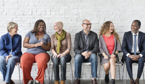 Diverse group of professionals seated in a horizontal row - women of color, men of color, women and men of different nationalities and orientations