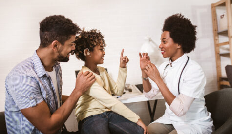 Father and child of color undergoing a friendly examination by a woman of color doctor in her office